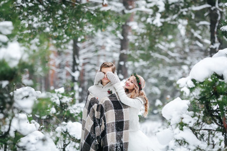 Cute girl covering boyfriends eyes by her knitted mittes. Winter wedding. Artwork.の写真素材