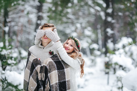 Cute girl covering boyfriend's eyes by her knitted mittes. Winter wedding. Artwork. Copy spaceの写真素材