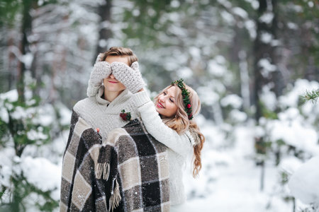 Cute girl covering boyfriends eyes by her knitted mittes. Winter wedding. Artwork.の写真素材