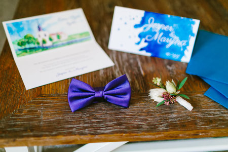 Stylish blue bow and boutonniere on wooden background next to blurred wedding invitation.の写真素材