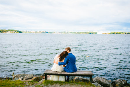 Newlyweds are relaxing on a bench and sitting before a river. Bride and groom is resting on natureの写真素材