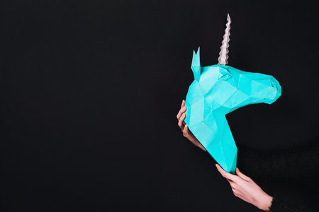 Hands hold a turquoise Unicorn. Artwork. 3d papercraft model of a unicorn. Copy spaceの写真素材