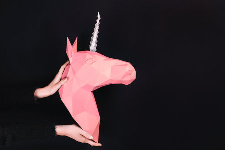 Hands hold a pink Unicorn. Artwork. 3d papercraft model of a unicorn. Copy spaceの写真素材