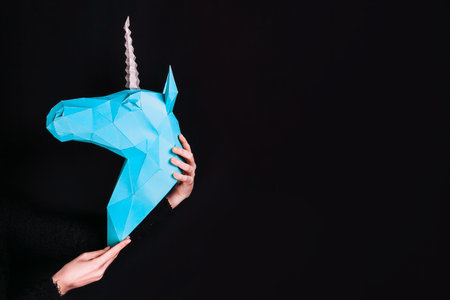 Hands hold a turquoise Unicorn. Artwork. 3d papercraft model of a unicorn. Copy spaceの写真素材
