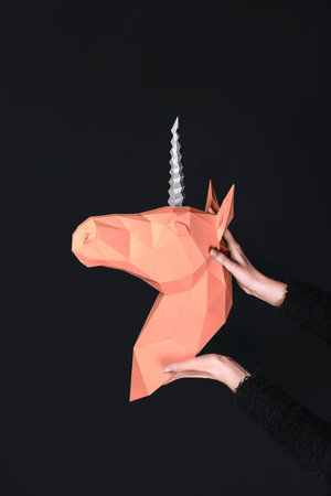 Hands hold a orange Unicorn. Artwork. 3d papercraft model of a unicorn. Copy spaceの写真素材