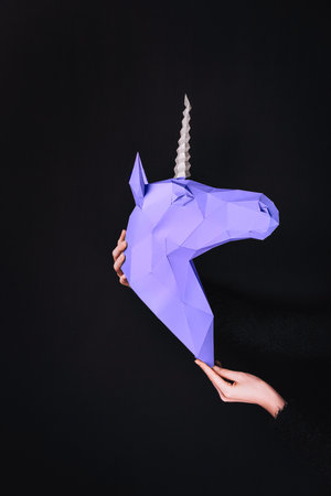 Hands hold a ultraviolet Unicorn. Artwork. 3d papercraft model of a unicorn. Copy spaceの写真素材