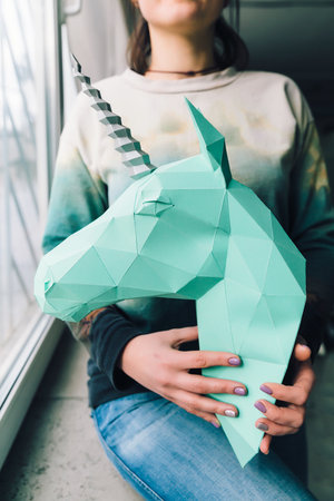 Girk holds a blue 3d model Unicorn on the windowsill. Artwork. Indoorの写真素材