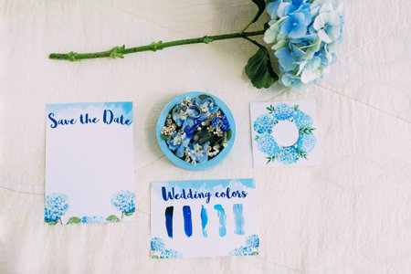 Wedding rings in blue box next to the Save The Date Invitation. Bridal flat lay in blue colors. Artworkの写真素材