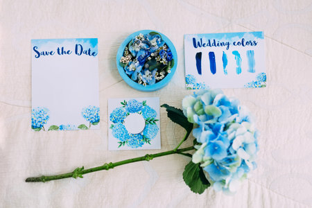 Wedding rings in blue box next to the Save The Date Invitation. Bridal flat lay in blue colors. Artworkの写真素材