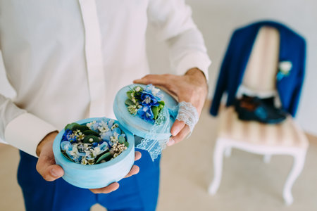 Groom holds a round box with Wedding rings with blue flowers. Artwork. Soft focus, Close-upの写真素材