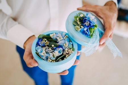 Groom holds a round box with Wedding rings with blue flowers. Artwork. Soft focus, Close-upの写真素材