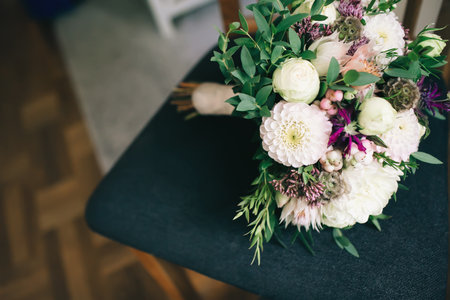 Rustic wedding bouquet with white dahlias, peonies, and greens on a dark chair. Artwork. Copy spaceの写真素材
