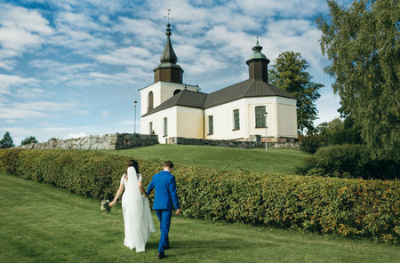 Wedding day. Bride and groom going to church through green field on blue sky backgrounds. Horizontalの写真素材