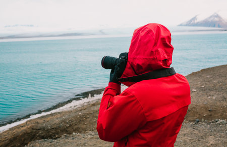 Nature travel photographer, person in red jacket taking photo of river in Iceland. Copy spaceの写真素材