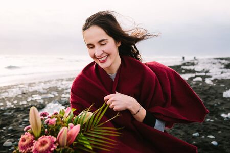 Cheerful bride under the plaid with a rustic on Black Sand Beach, Iceland. Artwork. Her hair shakes...
