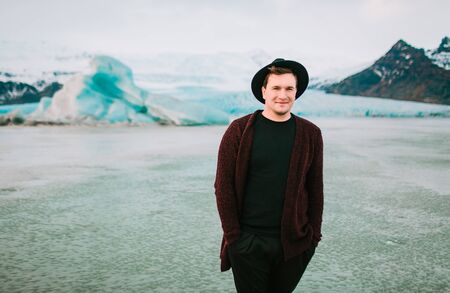 Smiling hipster in dark hat and casual clothes on glaciers background. Man look in camera. Copy spaceの写真素材