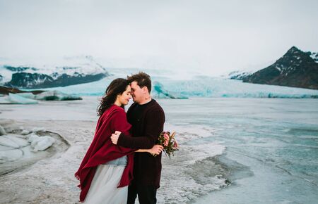 Stylish couple newlyweds smile and touching foreheads stand on background of glacier near Jokulsarlon in windy day. Copy spaceの写真素材