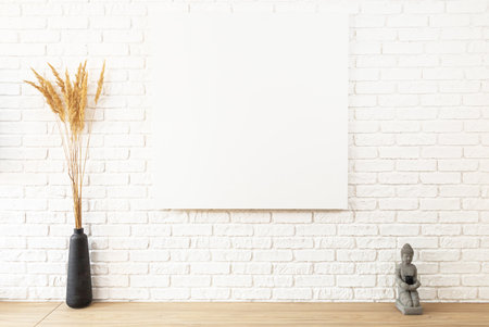 large white brick wall and canvas fragment in the center with place for text. Wooden table with black vase of decorative reeds and buddha statue with black candle. Mock up poster in loft interiorの写真素材