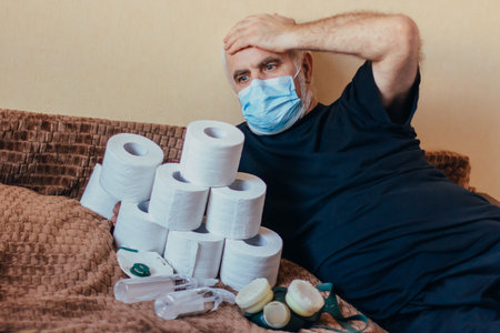 Senior man in face mask carrying a pile of toilet paper and clutching his head and worry about food deficiency and the high price of essential goods. shocked and surprised by the list of remediesの写真素材
