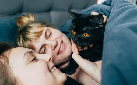 mother and daughter sleeps together in a bed with a black cat. Family spending time together. Close...