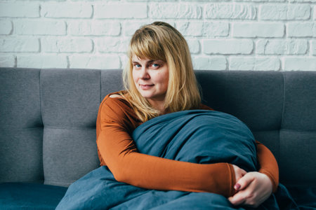 Thoughtful woman sitting on bed in bedroom and looking at camera. Portrait of middle aged woman smiling. Portrait of a beautiful middle aged woman at home. squint and mysteriously look. 
menopauseの写真素材
