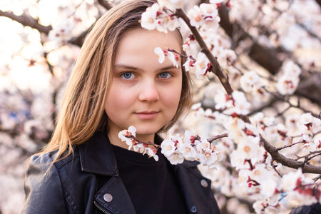 Portrait of hipster girl standing in spring blossom flowers garden and look at camera. Beautiful happy young woman enjoying smell in a flowering springtime vocation.の写真素材
