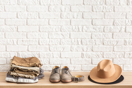 Men's casual outfits on wooden table over white brick wall background with place for text. Shoes, hat, belt and clothes. elegant male accessories. Minimalistic concept of home decor. の写真素材