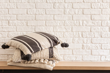 heap of cozy Colorful pillows on wooden oak shelf, on white bricks wall background. Minimalistic...