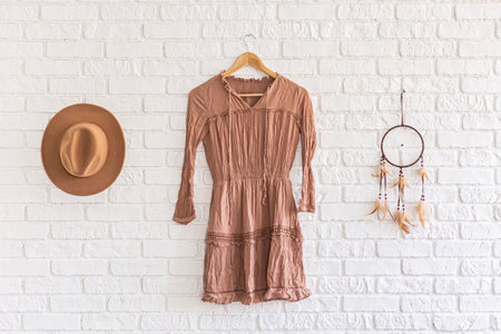 Fashion woman summer dress, hat and dream catcher hanging on white brick wall background. beautiful set clothes hanging on a hanger on a brick wall in a loft studio. Nobody. Showroomの写真素材