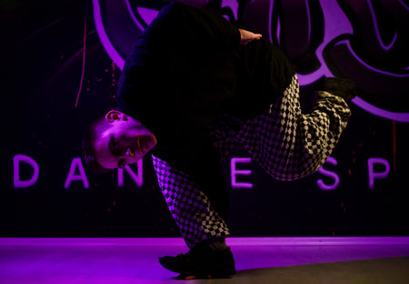 young guy dancer break dance shows his skill. doing an exercise. illuminated by a beautiful neon light.の写真素材