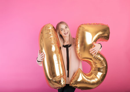 young happy girl holding large balloons in the form of the number fifteen on a pink background. holiday conceptの写真素材