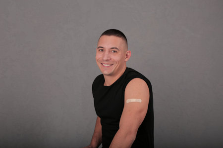 smiling young guy shows his hand after the vaccine. covid. the shoulder is covered with a plaster....
