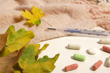 Thermometer, multicolored pills, yellow leaves and warm scarf. Autumn cold season concept.