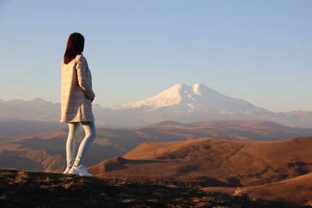 Back view of young woman in a coat admiring the view of Mount Elbrus. Inspiration nature.の写真素材