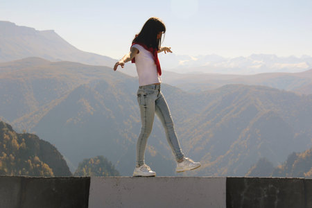 Young woman balancing on the edge of an abyss walks along the road parapet against the backdrop of...