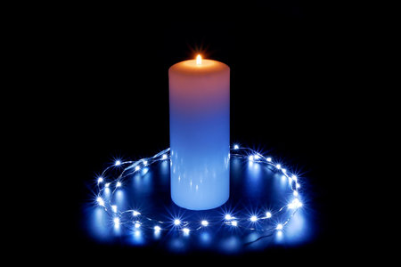 Burning candle in the illumination of lights on a dark black background.の写真素材