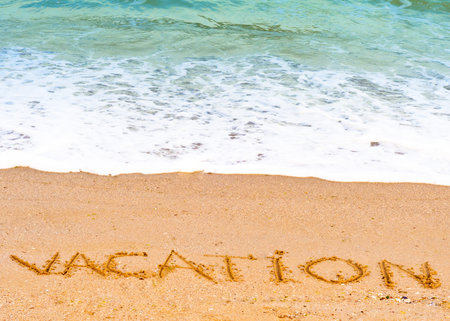 Vacation ; written in the sand on the beach blue waves in the background の写真素材