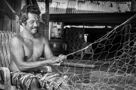 Koh Kood Island, Thailand - June 1, 2014: Thai fishermen mending his fishing net at Baan AoYai Salad fishing village on Koh Kood Island, Thailand.Fishing is the main occupation and income source on the islandのeditorial素材