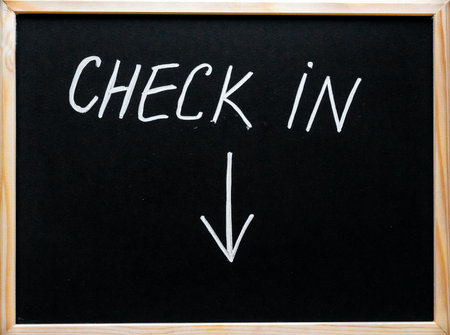 Check in message and arrow pointing downwards written with white chalk on wooden frame blackboardの写真素材