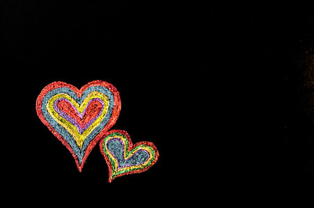 Conceptual image of love, with two vivid color shape hearts close one to each other .Vintage hand drawing on blackboard, isolated on black background, love concept, copy space availableの写真素材