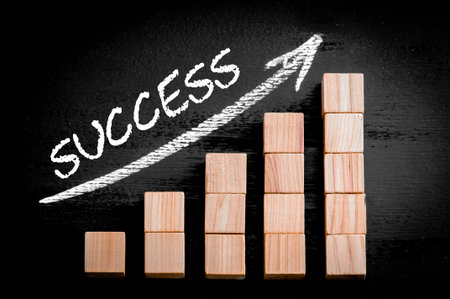 Word Success on ascending arrow above bar graph of Wooden small cubes isolated on black background.の写真素材