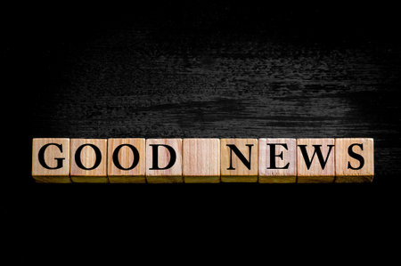 Message GOOD NEWS. Wooden small cubes with letters isolated on black background with copy space available. Concept image.の写真素材
