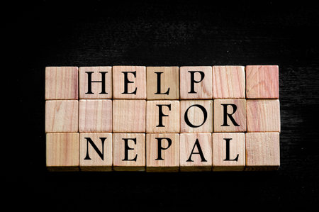 Message HELP FOR NEPAL isolated on black background. Wooden small cubes with letters isolated on...