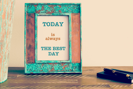 Retro effect and toned image of a vintage photo frame next to fountain pen and notebook . Motivational quote written with typewriter font TODAY IS ALWAYS THE BEST DAYの写真素材