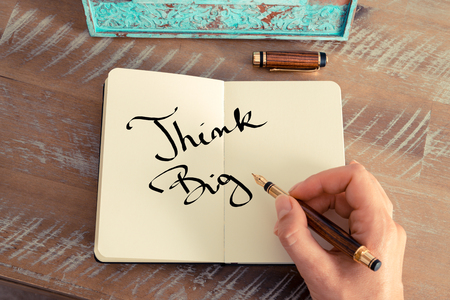 Retro effect and toned image of a woman hand writing a note with a fountain pen on a notebook. Motivational concept with handwritten text THINK BIGの写真素材