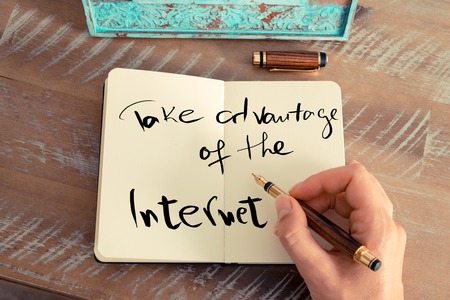 Retro effect and toned image of a woman hand writing a note with a fountain pen on a notebook. Handwritten text TAKE ADVANTAGE OF THE INTERNET, business success conceptの写真素材