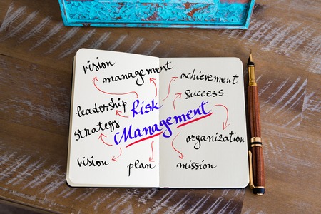 Retro effect and toned image of notebook next to a fountain pen. Business concept image with handwritten text RISK MANAGEMENTの写真素材