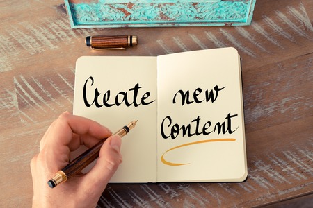 Retro effect and toned image of a woman hand writing a note with a fountain pen on a notebook. Handwritten text Create New Content as business concept imageの写真素材