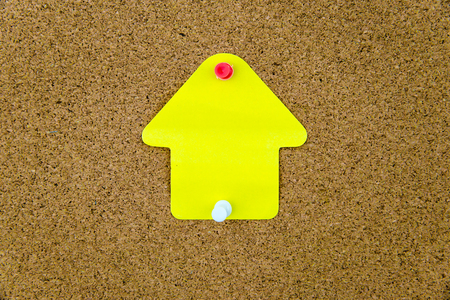 Blank yellow paper note in shape of house pinned on cork board with white and red thumbtacks, copy space availableの写真素材