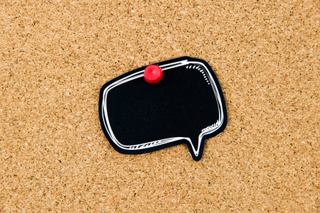 Empty black speech bubble pinned over cork board background, copy space available